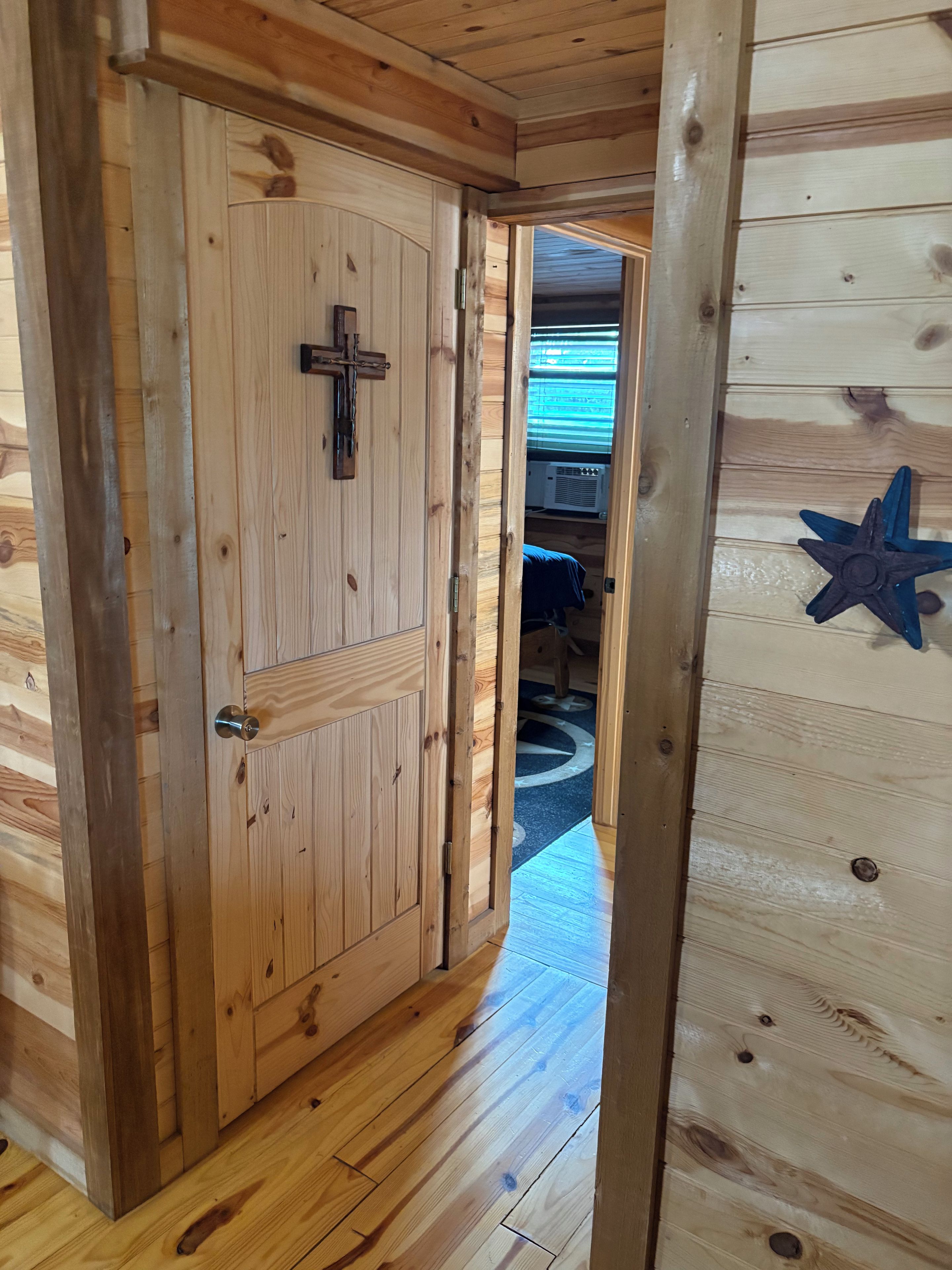 A wooden door with a cross, leading to a room with a bed and a star decoration on the wall.