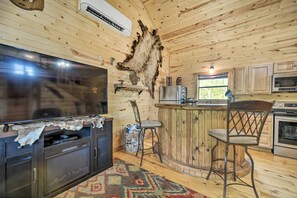 A rustic wooden interior with a bar area, a television, and a refrigerator. - Rustic Cabin On 31 Acres + Near the Frio River • Pet Friendly • Sleeps 6+ (Sabinal)