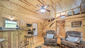 A wooden cabin interior with a kitchen, dining area, and seating. - Rustic Cabin On 31 Acres + Near the Frio River • Pet Friendly • Sleeps 6+ (Sabinal)