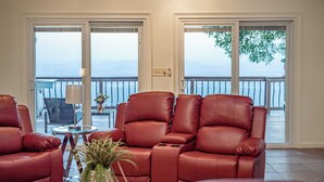 A room with a red leather sofa, a small table with a lamp, and a view of the sea through large sliding doors. - Panorama by Avantstay Unparalleled Views, Deck w/ Hottub, Game Room Pool Table (Sevierville)