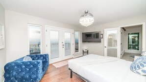 A bedroom with a bed, a TV, a chandelier, a blue chair, and a balcony door. - Panorama by Avantstay Unparalleled Views, Deck w/ Hottub, Game Room Pool Table (Sevierville)
