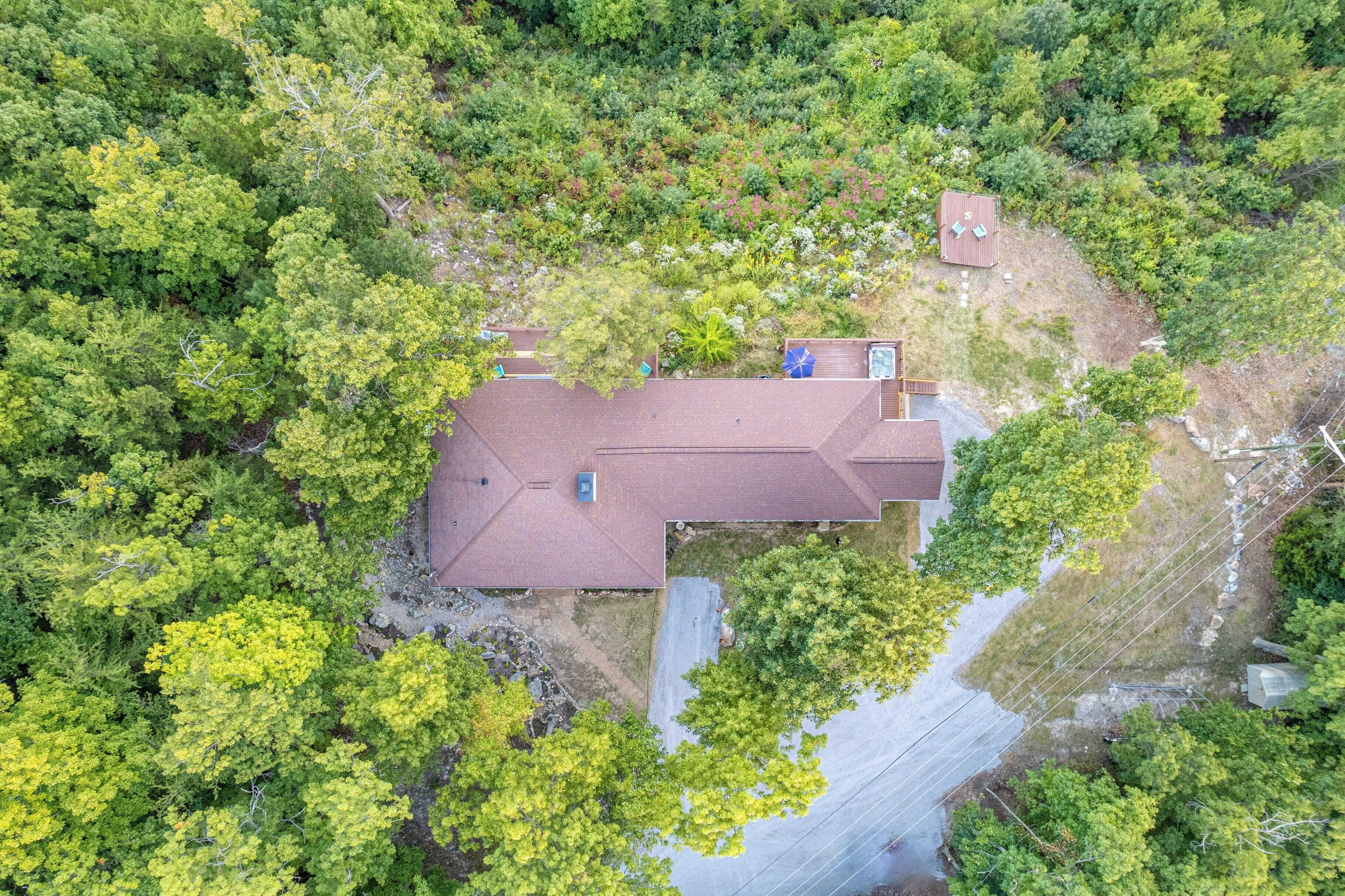 Une maison entourée d’une végétation luxuriante, avec un toit rouge et une petite terrasse.