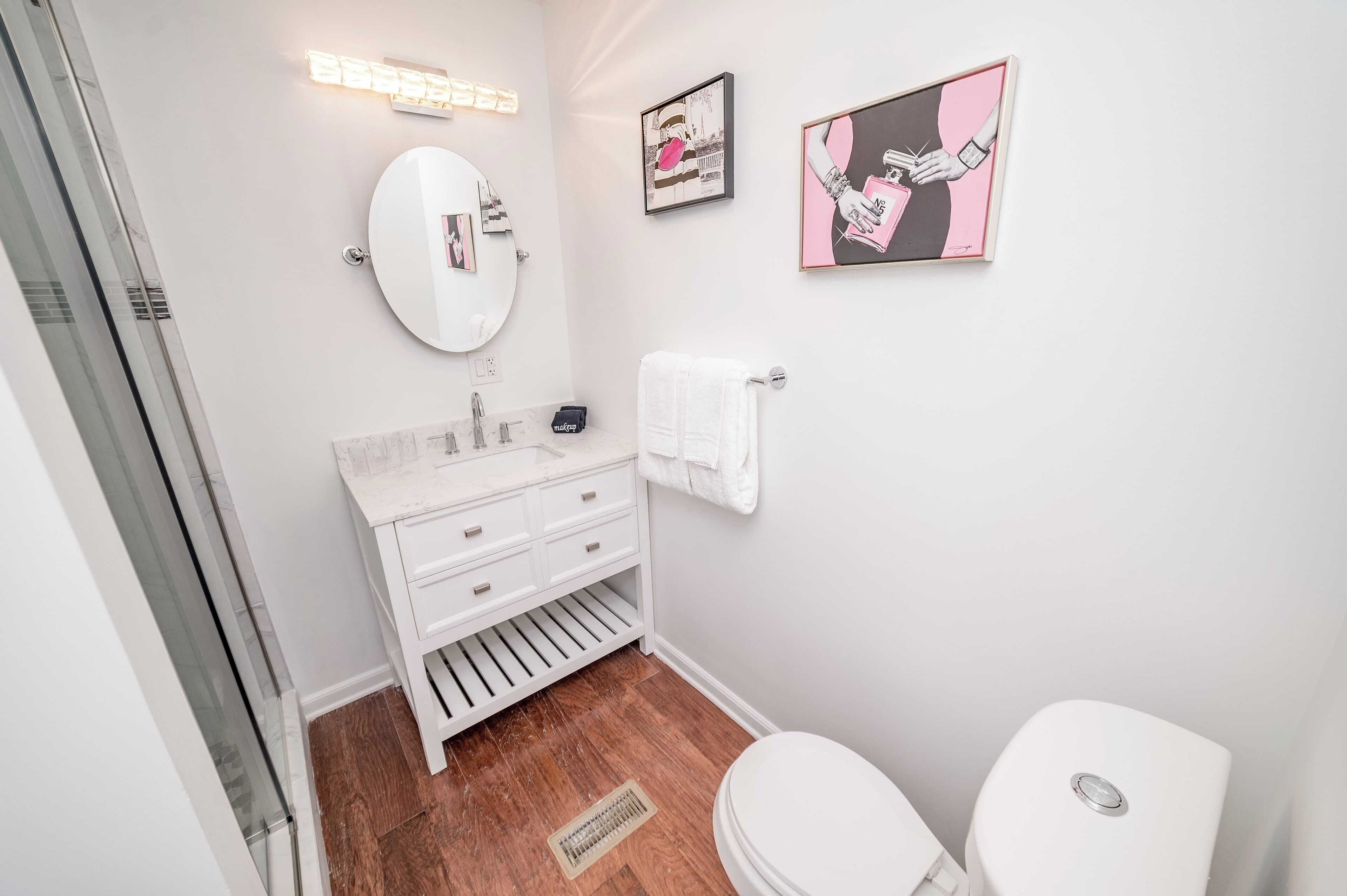 A modern bathroom with a white vanity, a round mirror, and two framed artworks on the wall.