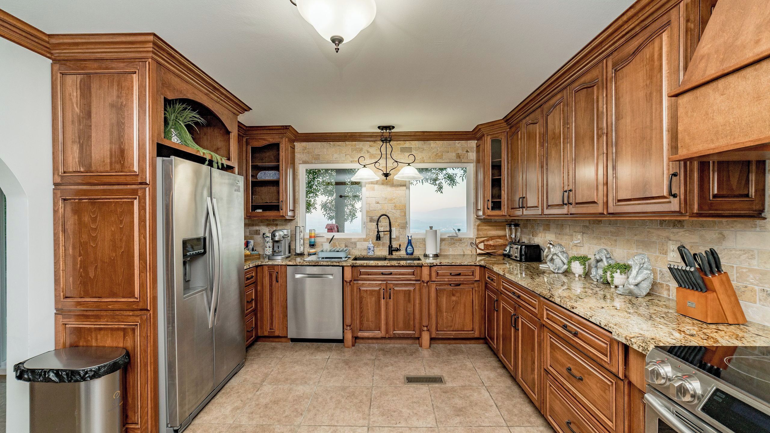 A kitchen with wooden cabinets, stainless steel appliances, a granite countertop, and a view through the window.