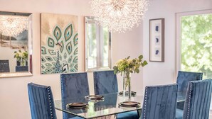 A dining area with a glass table surrounded by blue upholstered chairs, a chandelier, and artwork on the walls. - Panorama by Avantstay Unparalleled Views, Deck w/ Hottub, Game Room Pool Table (Sevierville)