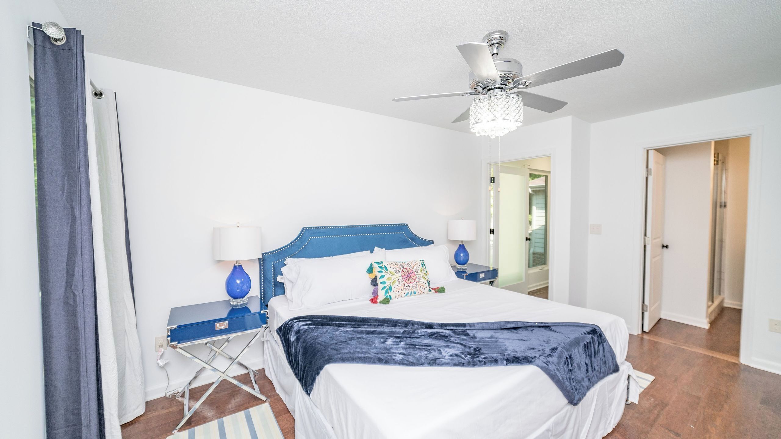 A bedroom with a bed, a ceiling fan, a nightstand, a lamp, and a suitcase.