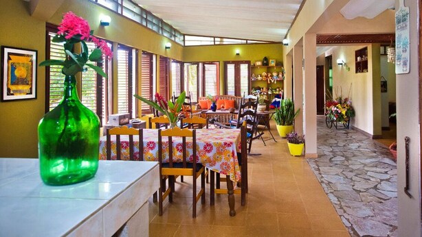 A dining area with a table set for four, surrounded by chairs, a green vase with flowers, and a window with blinds. - CASA VILLA ANACAHUITA ideal to be in contact with nature. (Limonal, Jarabacoa)