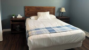 A neatly made bed with a plaid blanket, a wooden headboard, and a nightstand with a lamp and a tissue box. - 4 Bedroom Cottage- 129 Big Tub Rd (Tobermory)