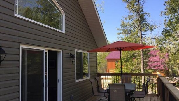 A deck with a table and chairs, a red umbrella, and a sliding glass door. - 4 Bedroom Cottage- 129 Big Tub Rd (Tobermory)