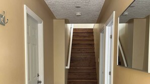 A hallway with a wooden staircase, white doors, and a black bench. - 4 Bedroom Cottage- 129 Big Tub Rd (Tobermory)