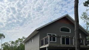 A two-story building with a covered porch and a gravel driveway. A sign indicates nearby locations: Escarpment, Heights, Cottage, and 129 Big Tub. - 4 Bedroom Cottage- 129 Big Tub Rd (Tobermory)