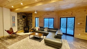 Een gezellige woonkamer met een stenen openhaard, een leren bank en grote ramen met uitzicht op een besneeuwd landschap.