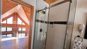 Een moderne badkamer met een glazen douchecabine, houten plafond en uitzicht op een houten terras.