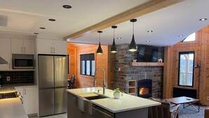 Een moderne keuken met roestvrijstalen apparatuur, een centraal eiland, hangende lampen en een stenen openhaard.