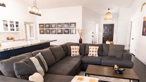 A modern living room with a sectional sofa, a coffee table, and a kitchen area with a marble countertop. - Spring training fields less than 10 miles, heated pool, e-bikes, sleeps 10 (Peoria)