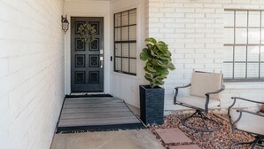 A covered porch with a dark door, a potted plant, and two chairs. - Spring training fields less than 10 miles, heated pool, e-bikes, sleeps 10 (Peoria)