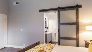 A bedroom with a bed, a sliding door, a nightstand, and a bathroom visible through an open door. - Spring training fields less than 10 miles, heated pool, e-bikes, sleeps 10 (Peoria)