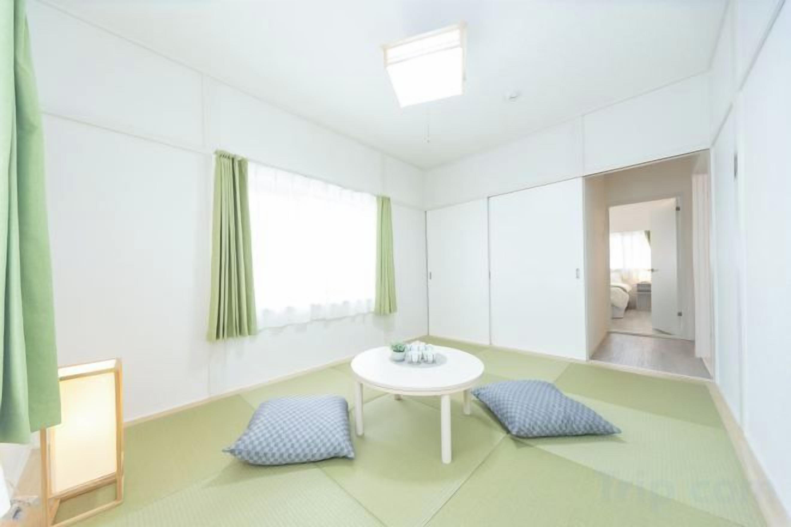 A room with tatami flooring, a round table, and a window with green curtains.