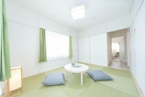 Una habitación con suelo de tatami, una mesa redonda y una ventana con cortinas verdes.