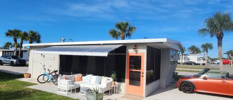 Et moderne sommerhus ved stranden med en overdækket terrasse, udendørs møbler og en cykel.