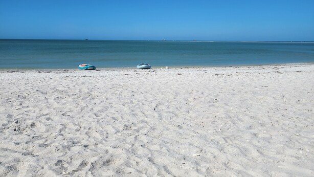 A beach with a clear sky, a sandy shore, and a blue water body in the distance.