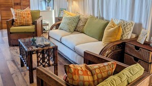 A cozy living room with a sofa, armchairs, a glass coffee table, and wicker side tables.