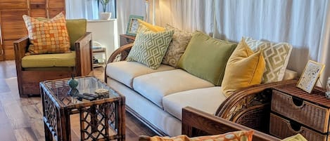 Una sala de estar acogedora con un sofá, sillones, una mesa de centro de vidrio y mesitas de noche de mimbre.