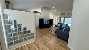 Ein modernes Wohnzimmer mit Holzboden, einem Fernseher auf einem schwarzen Standfuß, einem blauen Sofa und einer Glaswand mit Gitterstruktur.