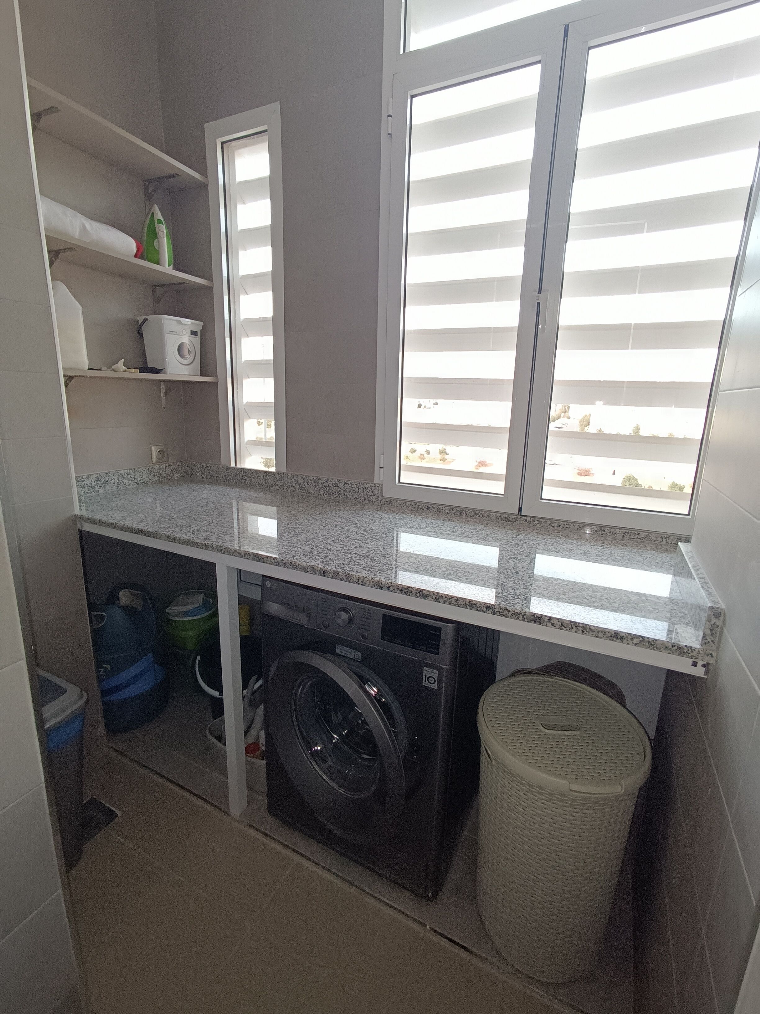 A compact laundry room with a washing machine, a drying rack, and a trash bin.