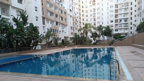 Ein Schwimmbecken, umgeben von einer angelegten Grünfläche mit Palmen und einem mehrstöckigen Wohngebäude im Hintergrund.
