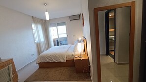 Ein Schlafzimmer mit einem Bett, einer Nachttischlampe und Blick auf einen Balkon durch ein Fenster.
