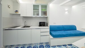 Cocina pequeña con armarios blancos, un tostador y un sofá azul.