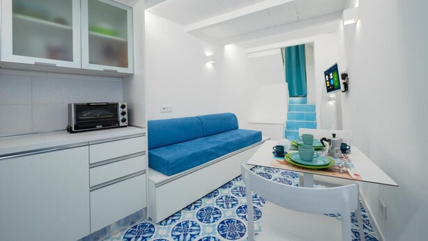 Una cocina compacta con microondas, un sofá azul y una mesa de comedor con una silla.