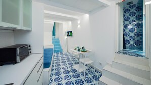 Una cocina moderna con horno empotrado, un pequeño comedor con mesa y sillas, y un baño con ducha y paredes de azulejos.