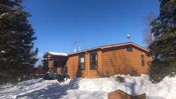 A wooden cabin with a sloped roof, surrounded by snow and trees.