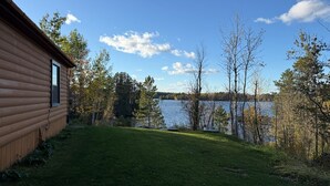 A log cabin with a grassy yard and a lake view.