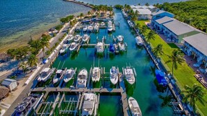 An aerial view of a marina with numerous boats docked, surrounded by lush greenery and a clear blue sky.