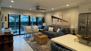 A modern living room with a sofa, chairs, a coffee table, and a kitchen area with a refrigerator.