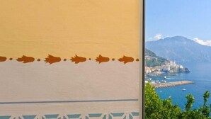 A coastal town with buildings along the waterfront, a clear sky, and mountains in the background. - AMALFI "Casa Dipinta" SEA VIEW APT (AMALFI)
