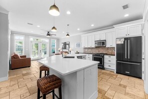 Una cocina amplia con armarios blancos, una isla grande y un refrigerador negro.