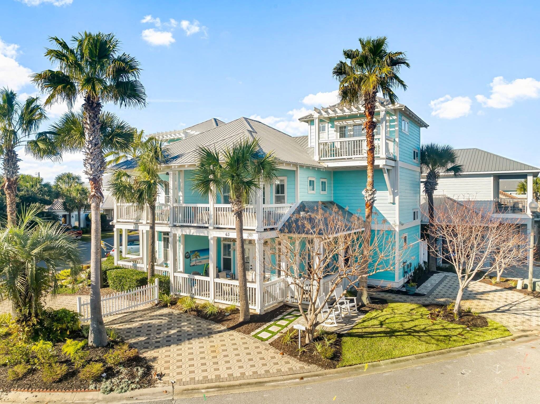 A two-story house with a balcony, surrounded by palm trees and a well-maintained lawn.
