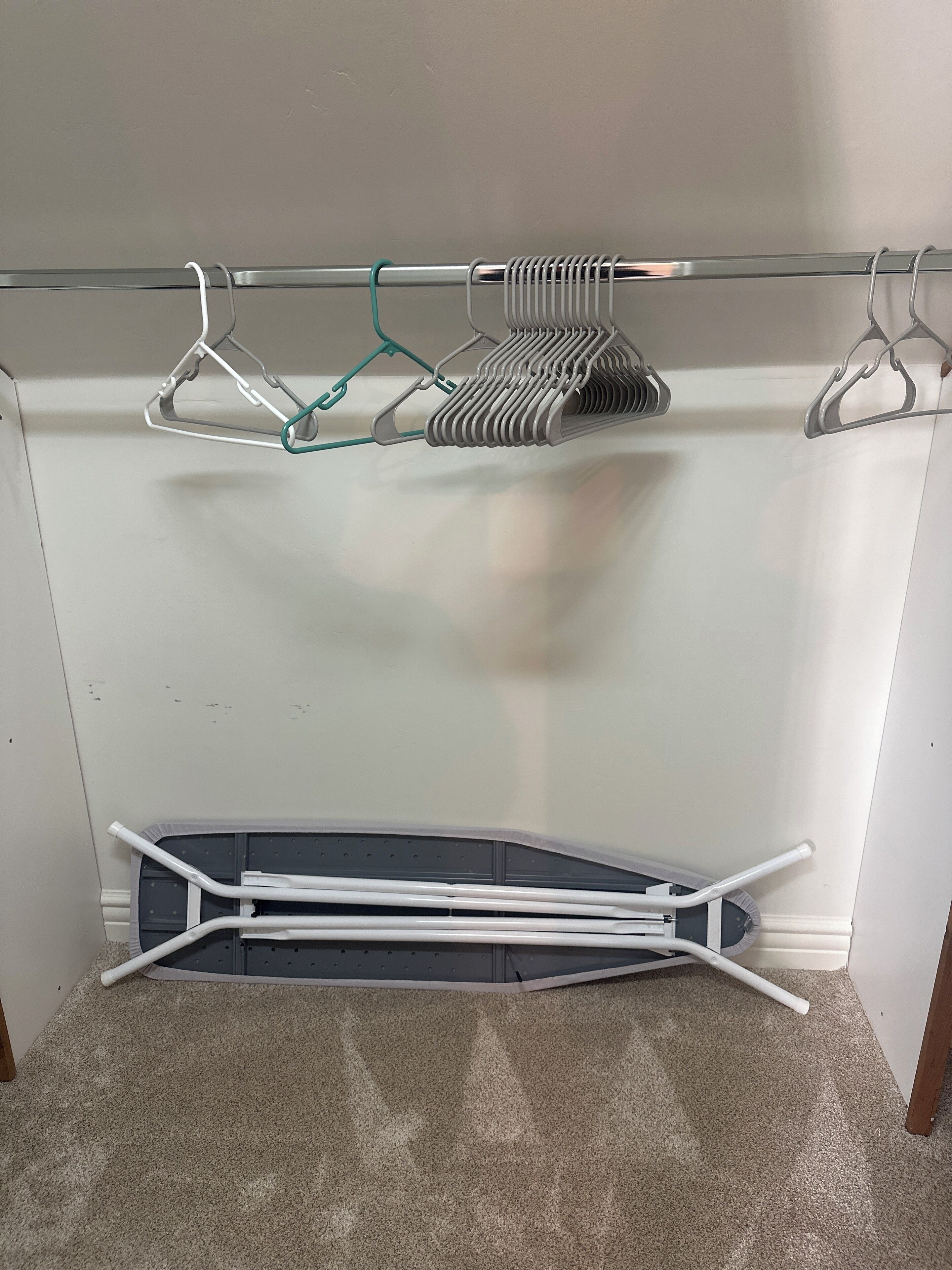 Een kamer met een glazen strijkplank, een metalen rek met ophanghaakjes en een witte strijkplank.