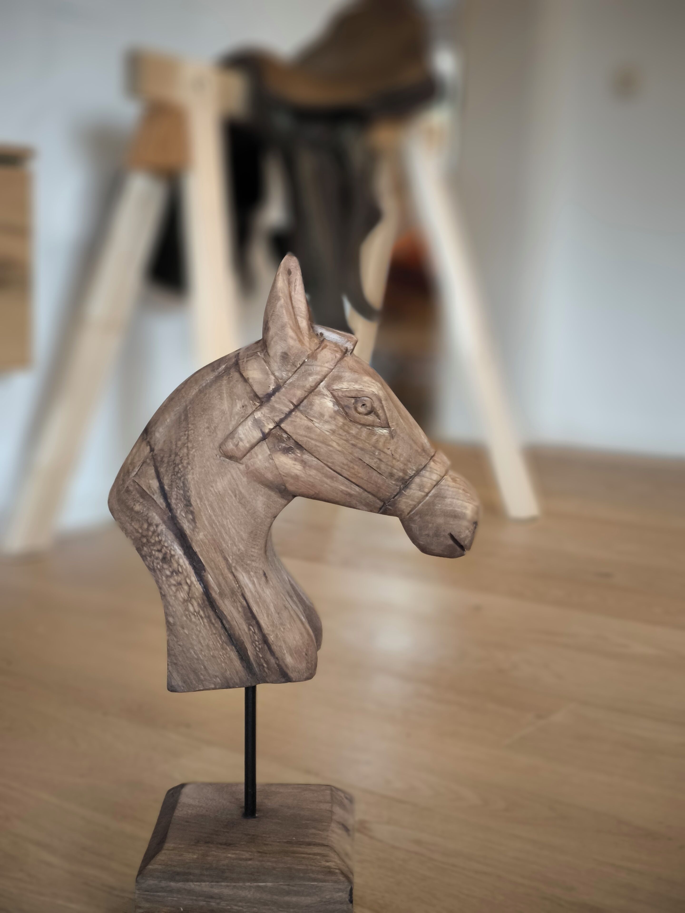Escultura de cabeça de cavalo de madeira sobre um suporte.