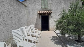 A building with a stone facade, a tiled entrance, and outdoor seating with white chairs. - Country house for rent in 7700 St-Marcel d'Ardèche (Saint-Marcel-d'Ardèche)