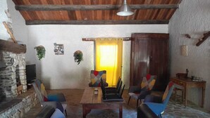A rustic interior with a stone fireplace, wooden ceiling beams, and a dining area with a table and chairs. - Country house for rent in 7700 St-Marcel d'Ardèche (Saint-Marcel-d'Ardèche)