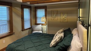 Un dormitorio con cama, vigas de madera, ventanas con persianas y cuadros en la pared.
