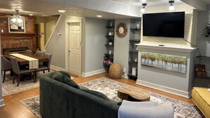 Una sala de estar con chimenea, televisor montado encima y comedor con mesa y sillas.