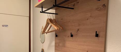 A room with a wooden wall-mounted rack holding a plant, a mirror, and a coat hanger.