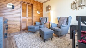 A cozy living room with two grey armchairs, a small table, and a wooden wall with a mirror and wall art.