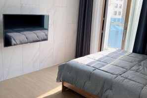 A bedroom with a bed, a mounted TV, and a window with curtains. - Jeju (Shinjeju) House (Jeju City)